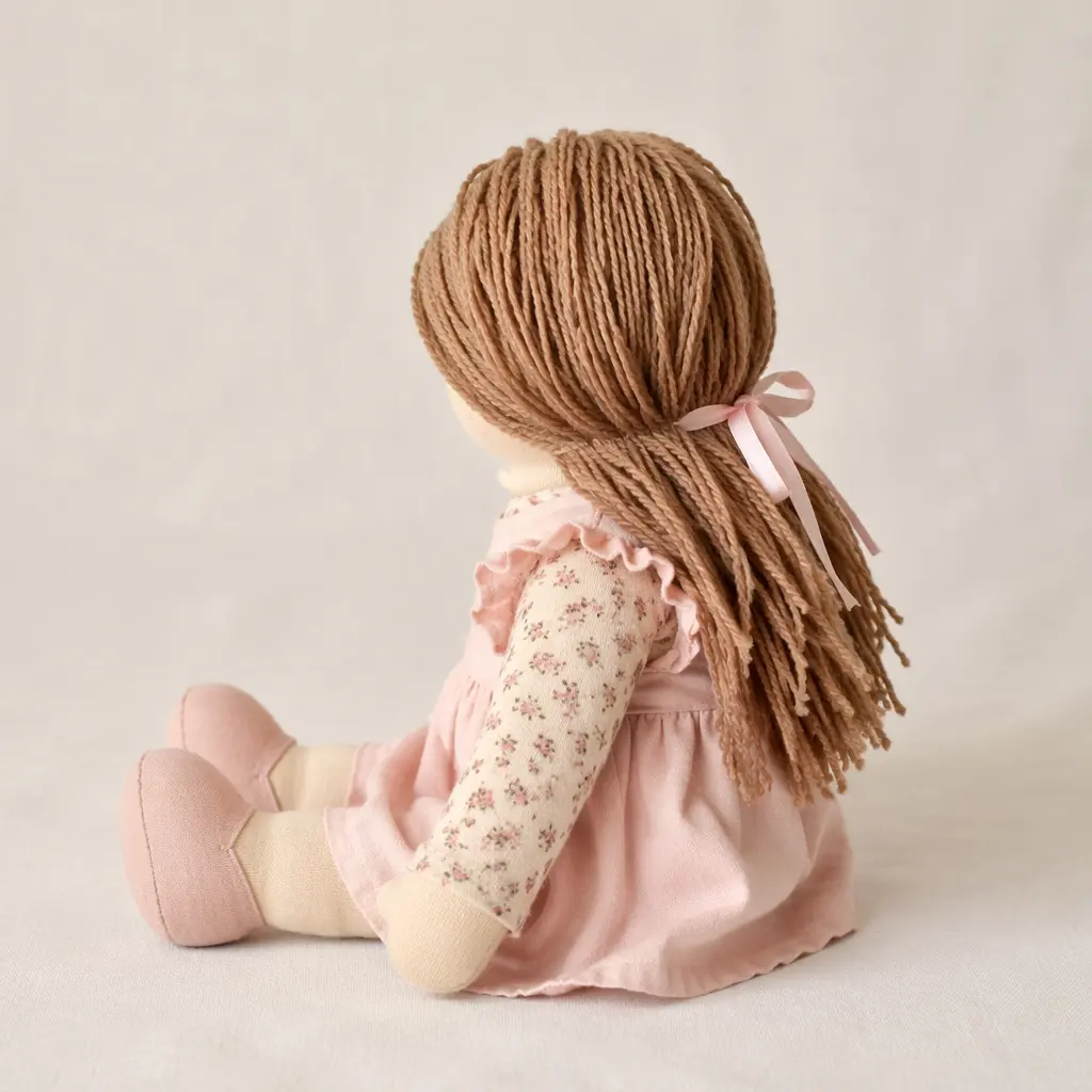 A soft-bodied classic-style doll shown from the side, highlighting its fabric body and yarn hair