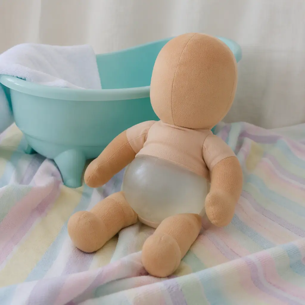 Soft-bodied water-filled baby doll resting beside a toy bathtub in a softly lit studio scene